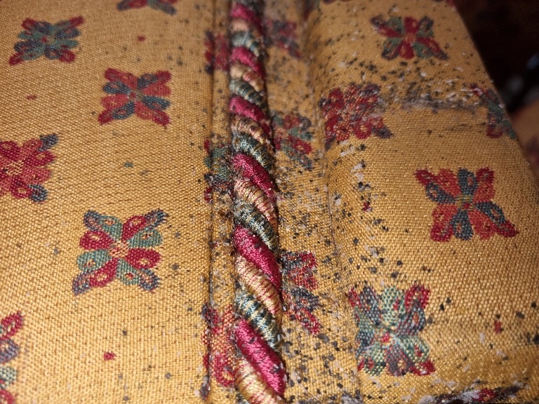 Tissu jaune à motifs rouges et verts, cordon torsadé, points noirs denses et petits grains clairs le long du cordon